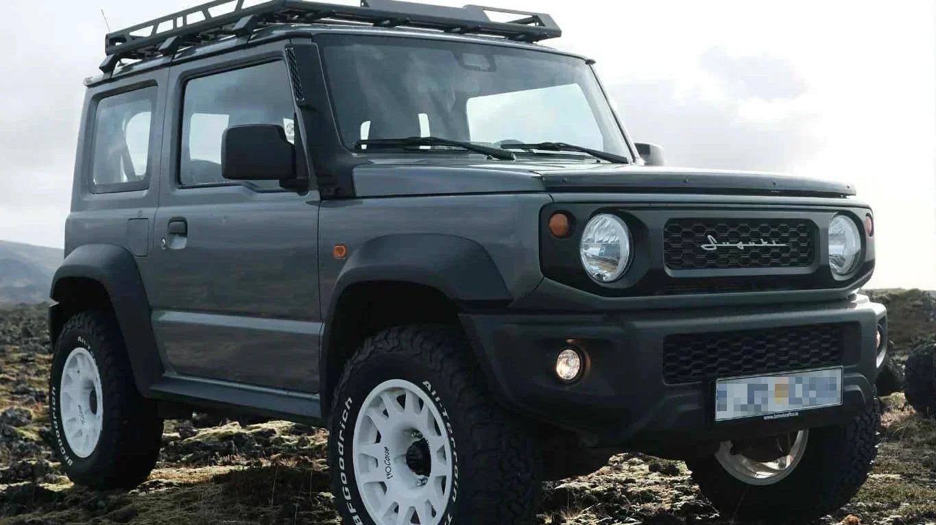 Suzuki Jimny (2018+) with 16" EVO Corse DakarZero wheels in white mounted on BF Goodrich KO2 tyres and various accessories such as retro grille and vintage emblem.